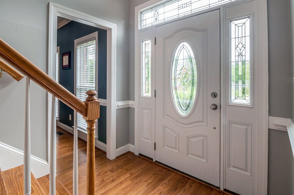 Bright and inviting home entrance featuring a white door with intricate stained glass and wooden flooring.